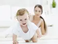 Bebé sonriente gateando, con su madre observando. Una escena tierna para estimular el gateo.