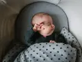 Bebé durmiendo abrigado con un mono gris y manta de corazones. Ideas para como vestir a un recien nacido en junio.