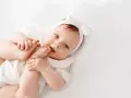 Bebé con diadema de lazo blanco, jugando con sus pies. El significado de Gorka es "pastor", como este bebé cuidando sus pequeños pies.