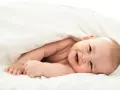 Un bebé sonriente se asoma bajo una manta blanca. Parece que los bebes tienen memoria, ¡y este ya recuerda cómo sonreír!