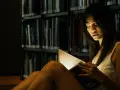 Elena, in the library's dim light, engrossed in a book.
