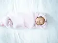 Bebé recién nacido envuelto en manta rosa, durmiendo plácidamente. La temperatura de la casa es ideal para el bebé.