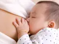 Bebé asiático durmiendo mientras se alimenta, mostrando el reflejo de succión. Su mano pequeña descansa sobre el pecho de su madre.