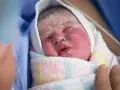 Recién nacido envuelto en una manta, con la piel rosada y cubierta de vernix bebe. Una mano lo acaricia suavemente.