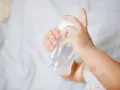 Manitas de bebé sujetando un biberón. Se aprecian rojeces en su piel, quizás por dermatitis o por el calor del sudor.