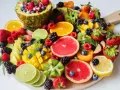 Tabla de frutas de primavera: piña, naranjas, fresas, frambuesas, moras, arándanos, mango, kiwi, pomelo y limón.