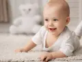 Un bebé sonriente y con ojos azules empieza a reptar sobre una alfombra mullida, explorando el mundo.