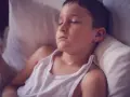 Un niño duerme con la cabeza sudada, quizás por una fiebre o porque un niño suda mucho la cabeza al dormir.