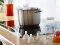 Preparación para desinfectar biberones con agua hirviendo. Tetinas y un biberón medidor listos en la encimera.