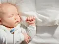 Bebé de 1 mes durmiendo con termómetro que marca 38.2°C, indicando un posible resfriado.