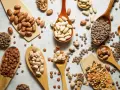Cucharas de madera repletas de legumbres bebes: lentejas, garbanzos y frijoles de diversos tipos, esparcidos sobre una superficie clara.