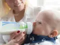 Una madre sonriente enseña como dar el biberón a su bebé, quien succiona felizmente.