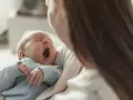 Bebé bosteza en brazos de su madre. Podría ser un signo de hipoglucemia bebé, pero también solo sueño.