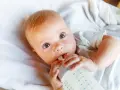 Bebé con ojos grandes y curiosos, bebiendo leche de un biberón. La imagen responde a la pregunta: cuanta leche toma un bebe.