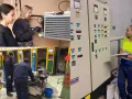 Alazne nombre, aprendiendo mecánica. Mujeres trabajando en un taller, revisando un panel de control y un equipo de refrigeración.