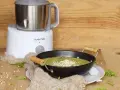 Un puré verde cremoso, ideal para nabo bebés, servido en un cuenco negro con garbanzos y hierbas. Al fondo, una máquina de cocina Suavinex.