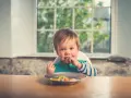 Un bebé con babero verde come felizmente de un plato. Parece que está disfrutando de su comida, quizás marisco para bebés.