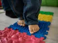 Pies descalzos de un niño sobre un tapete de rompecabezas texturizado, parte de juegos de coordinación para el desarrollo.