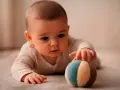 Bebé concentrado, explorando el mundo cuando empiezan a coger cosas. Toca una pelota de tela con sus manitas.