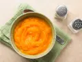 Puré de calabaza y patata para bebé, listo para congelar. Servido en un cuenco con una cuchara y saleros al lado.