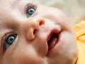 Bebé con ojos azules y boca abierta, mostrando las encías y los primeros dientes saliendo.