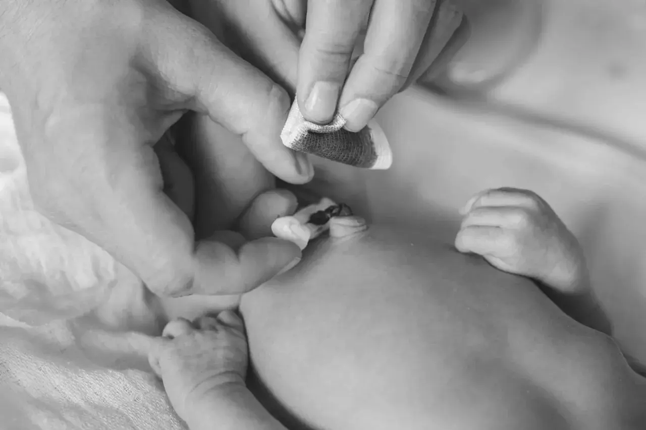 Manos cuidadosas limpian el cordón umbilical de un recién nacido con una gasa.