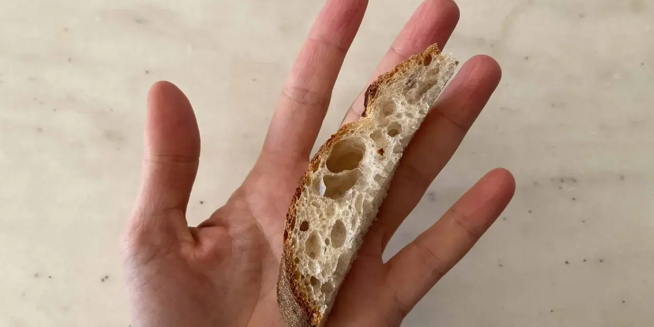 Una mano sostiene una rebanada de pan artesanal, perfecta para el primer pan para bebés.