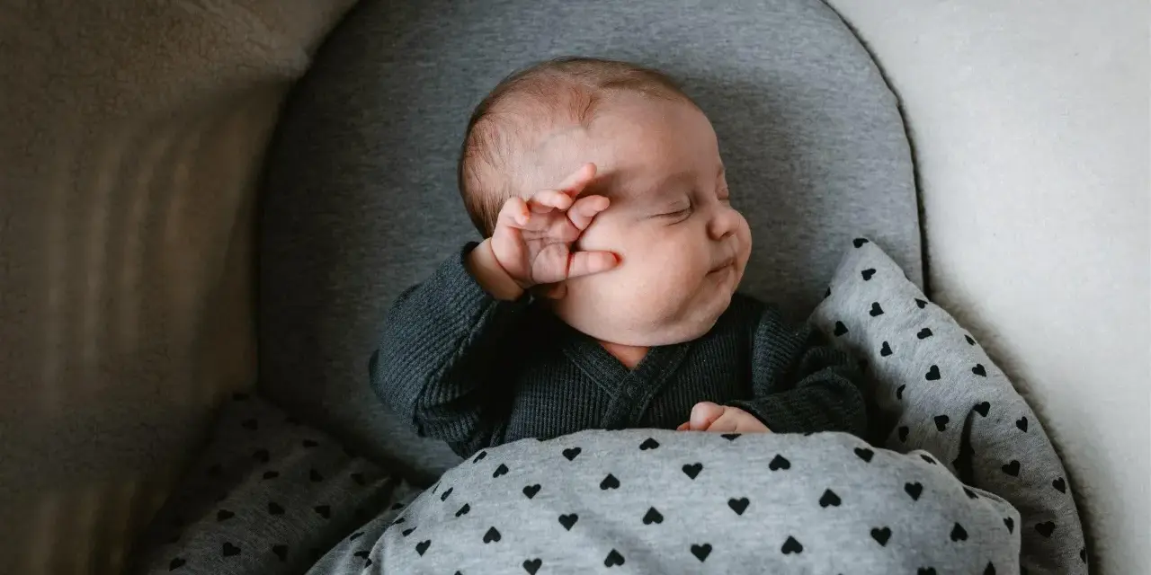 Bebé durmiendo abrigado con un mono gris y manta de corazones. Ideas para como vestir a un recien nacido en junio.