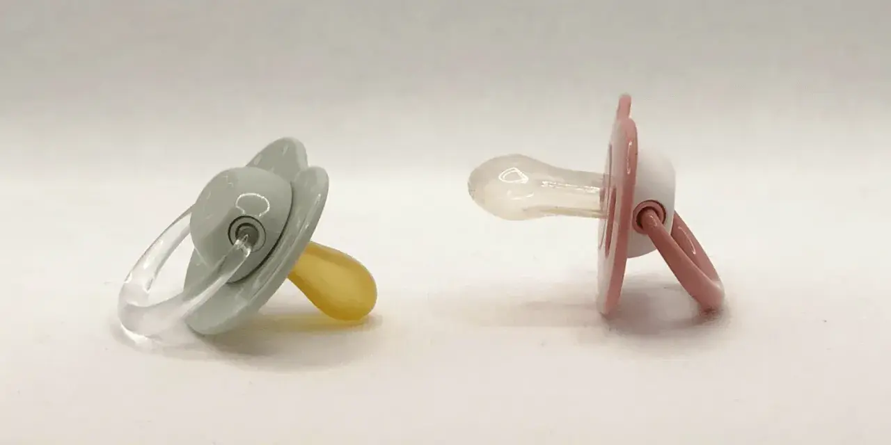 Dos chupetes, uno gris con tetina de látex y otro rosa con tetina de silicona, esperan a ser elegidos.