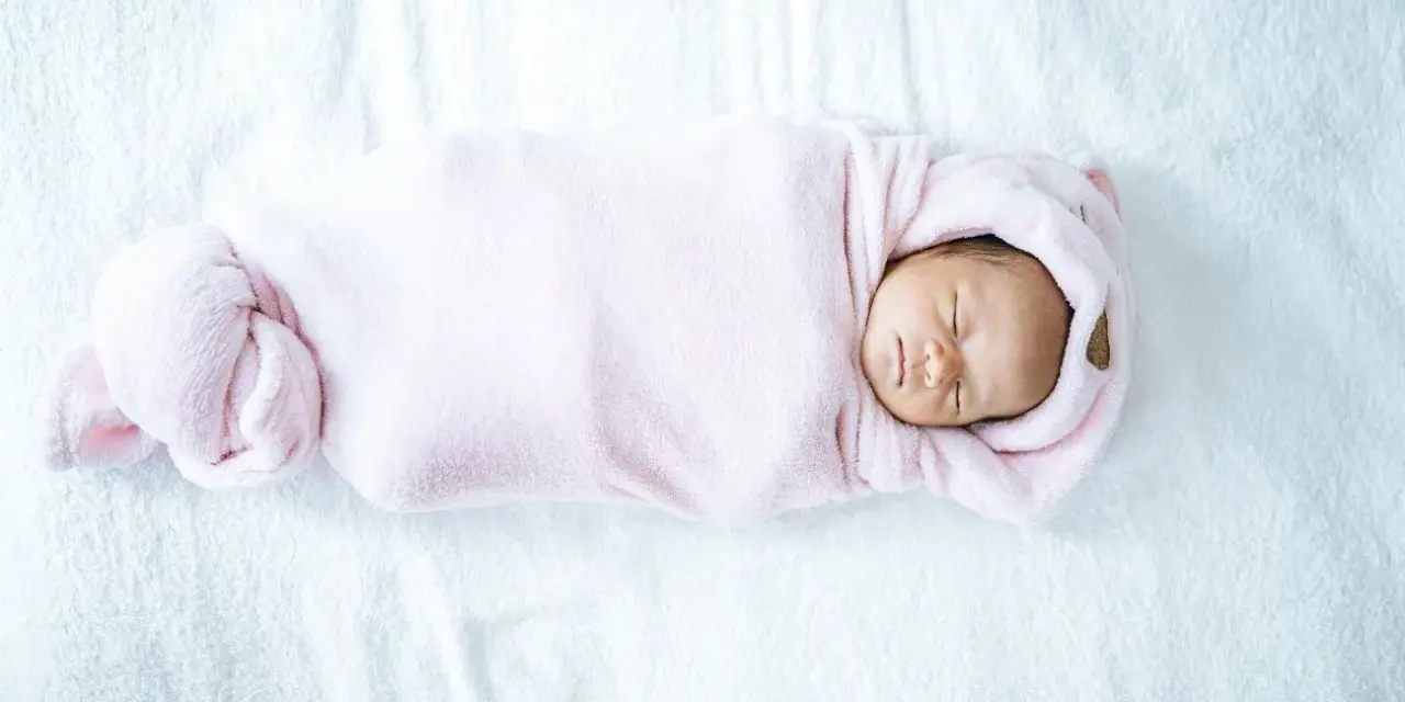 Bebé recién nacido envuelto en manta rosa, durmiendo plácidamente. La temperatura de la casa es ideal para el bebé.