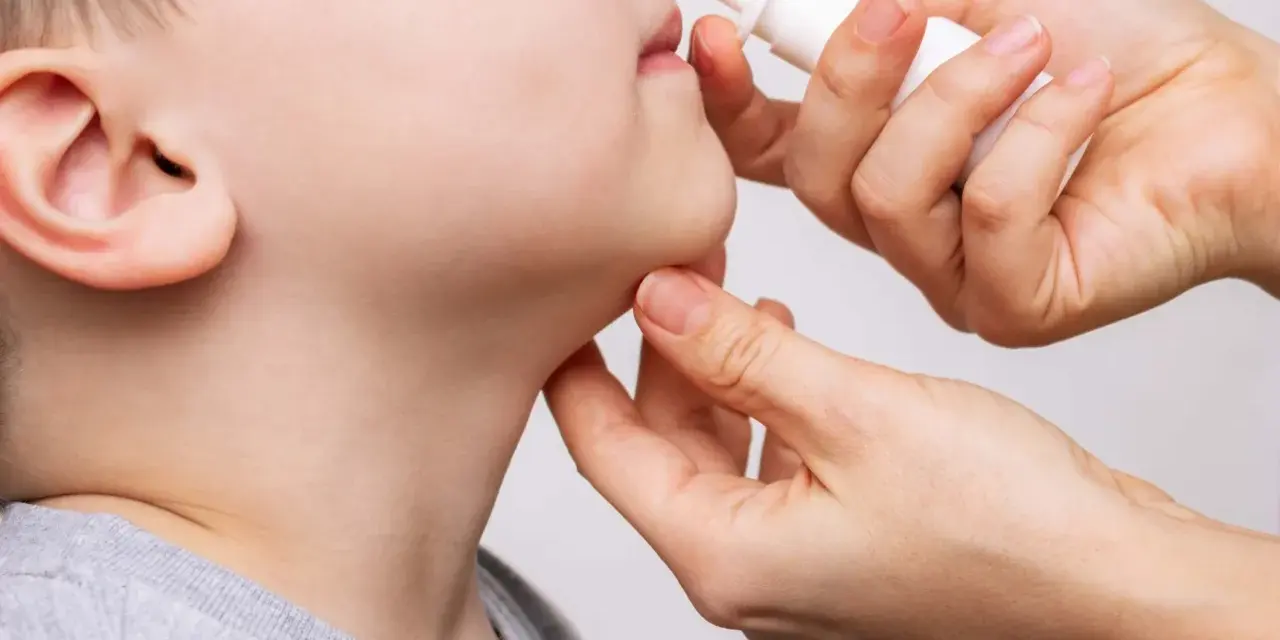 Una mano aplica spray nasal a un niño. La imagen ilustra cuántos lavados nasales se pueden hacer a un bebé para aliviar la congestión.
