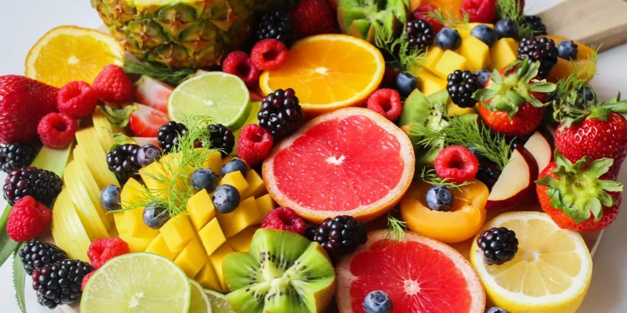Tabla de frutas de primavera: piña, naranjas, fresas, frambuesas, moras, arándanos, mango, kiwi, pomelo y limón.