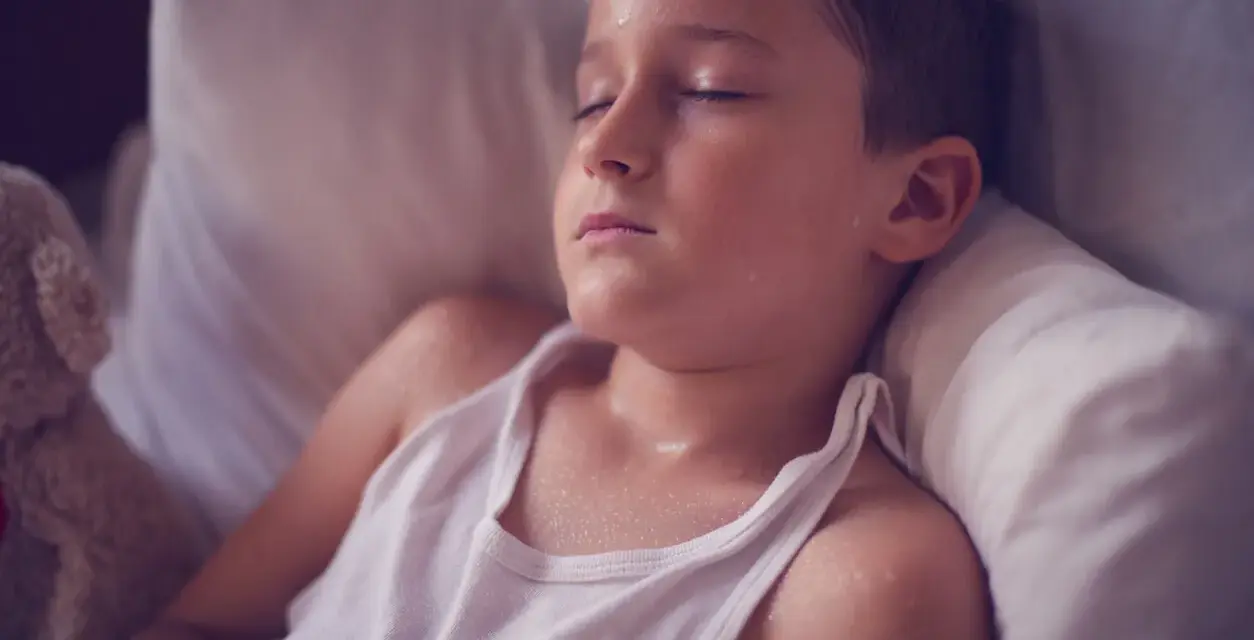 Un niño duerme con la cabeza sudada, quizás por una fiebre o porque un niño suda mucho la cabeza al dormir.