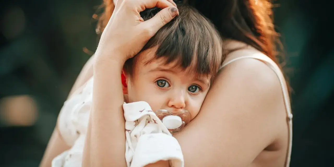 Bebé con chupete, acurrucado en brazos de su madre. Un momento tierno que nos hace pensar en cuando se inventó el chupete.