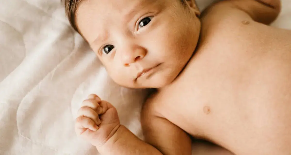 Bebé con mirada intensa, su puño cerrado y piel suave. Podría ser un signo de hipertonía en bebés, pero su expresión es serena.
