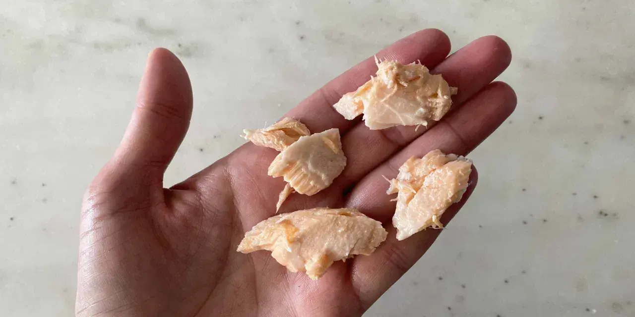 Trozo de salmón desmenuzado en una mano, ideal para saber cuándo dar salmón a un bebé.