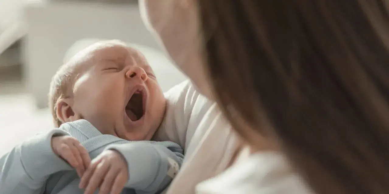 Bebé bosteza en brazos de su madre. Podría ser un signo de hipoglucemia bebé, pero también solo sueño.