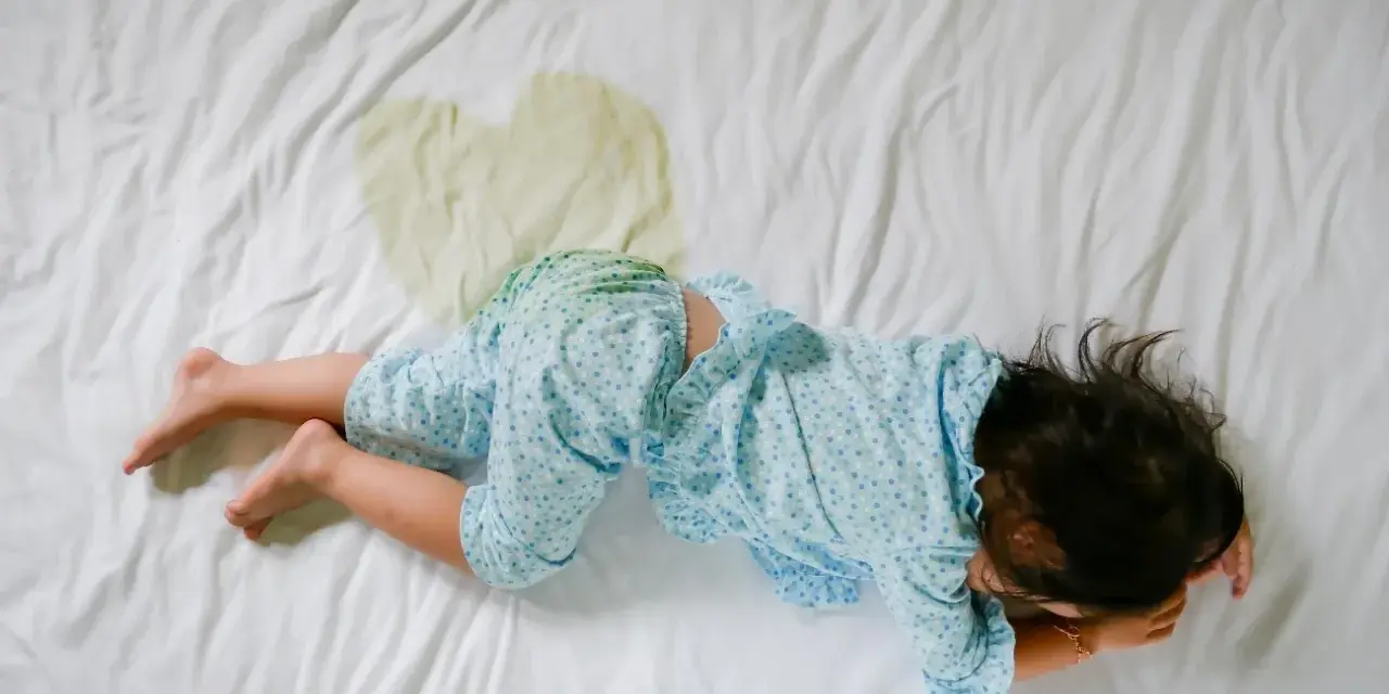 Niño en cama con mancha de orina. Buscando enuresis nocturna infantil remedios naturales para ayudarle.