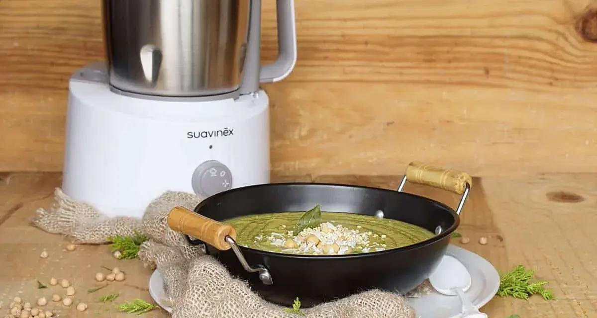 Un puré verde cremoso, ideal para nabo bebés, servido en un cuenco negro con garbanzos y hierbas. Al fondo, una máquina de cocina Suavinex.