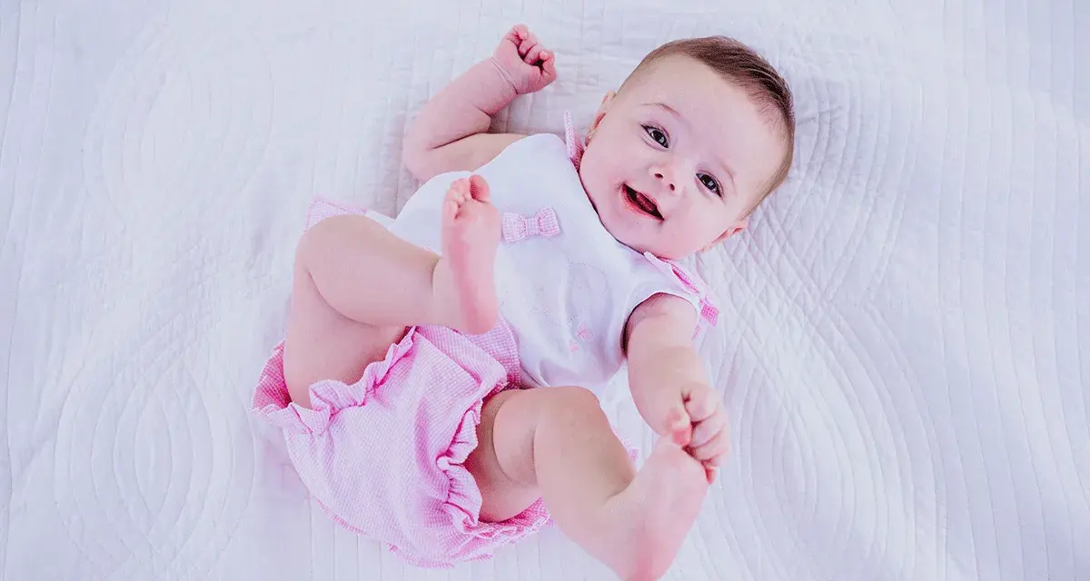 Bebé sonriente con un traje rosa y blanco, perfecto para inspirar nombres de niñas.