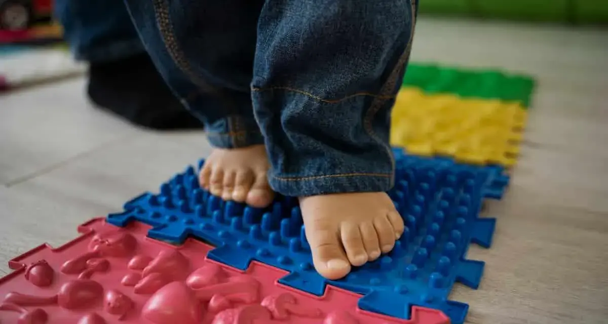 Pies descalzos de un niño sobre un tapete de rompecabezas texturizado, parte de juegos de coordinación para el desarrollo.