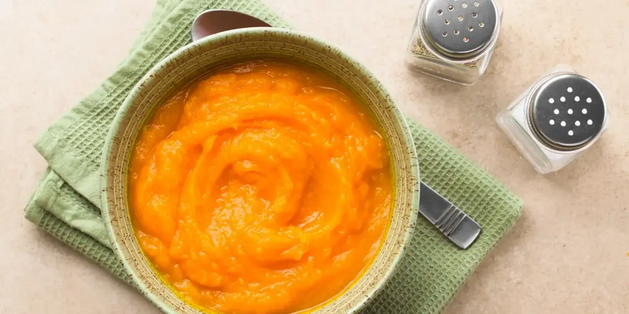 Puré de calabaza y patata para bebé, listo para congelar. Servido en un cuenco con una cuchara y saleros al lado.