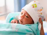 Bebé envuelto en manta con ballenas, con gorrito de pájaros, mirando con curiosidad. El momento en que un bebé reconoce a sus abuelos.