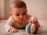 Bebé concentrado, explorando el mundo cuando empiezan a coger cosas. Toca una pelota de tela con sus manitas.