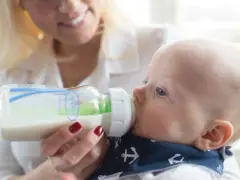 Una madre sonriente enseña como dar el biberón a su bebé, quien succiona felizmente.