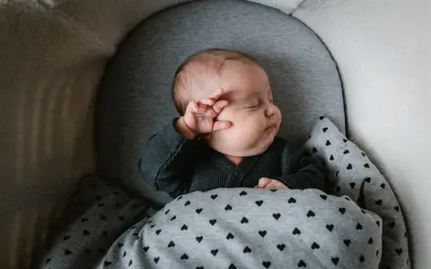 Bebé durmiendo abrigado con un mono gris y manta de corazones. Ideas para como vestir a un recien nacido en junio.
