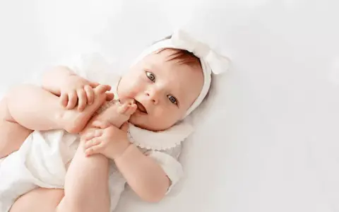 Bebé con diadema de lazo blanco, jugando con sus pies. El significado de Gorka es "pastor", como este bebé cuidando sus pequeños pies.