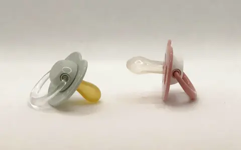 Dos chupetes, uno gris con tetina de látex y otro rosa con tetina de silicona, esperan a ser elegidos.