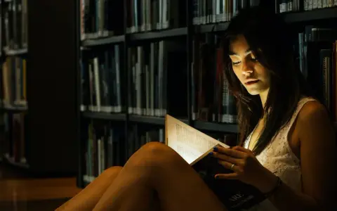 Elena, in the library's dim light, engrossed in a book.