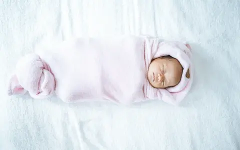 Bebé recién nacido envuelto en manta rosa, durmiendo plácidamente. La temperatura de la casa es ideal para el bebé.